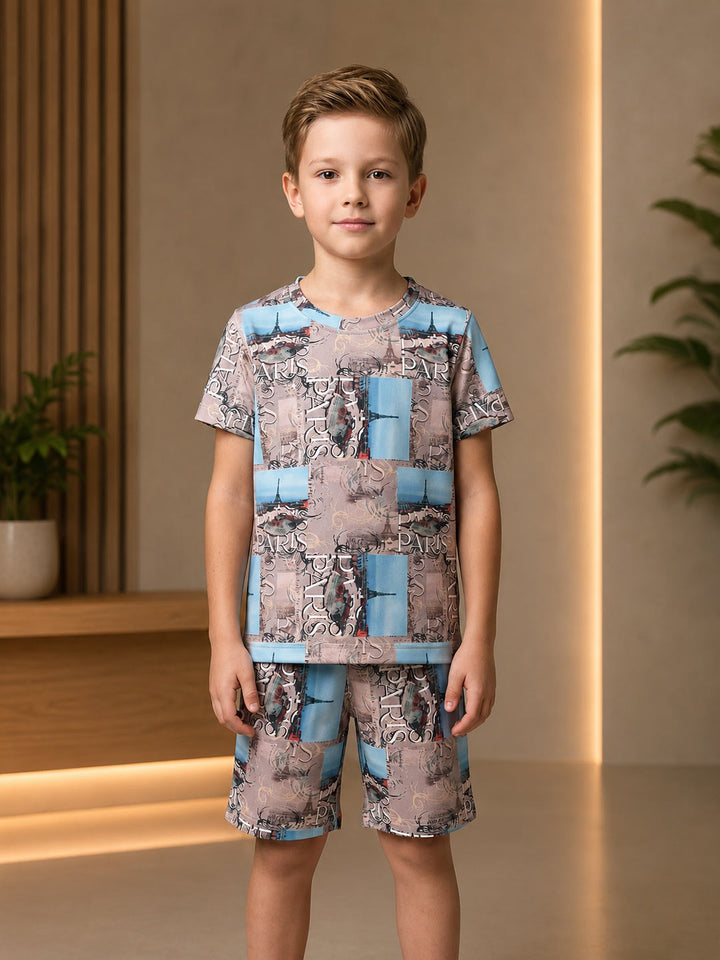 A young boy stands in a modern indoor setting wearing a matching short-sleeve t-shirt and shorts set. The set features a patchwork-style print combining snakeskin and abstract patterns in shades of gray, beige, and light blue.