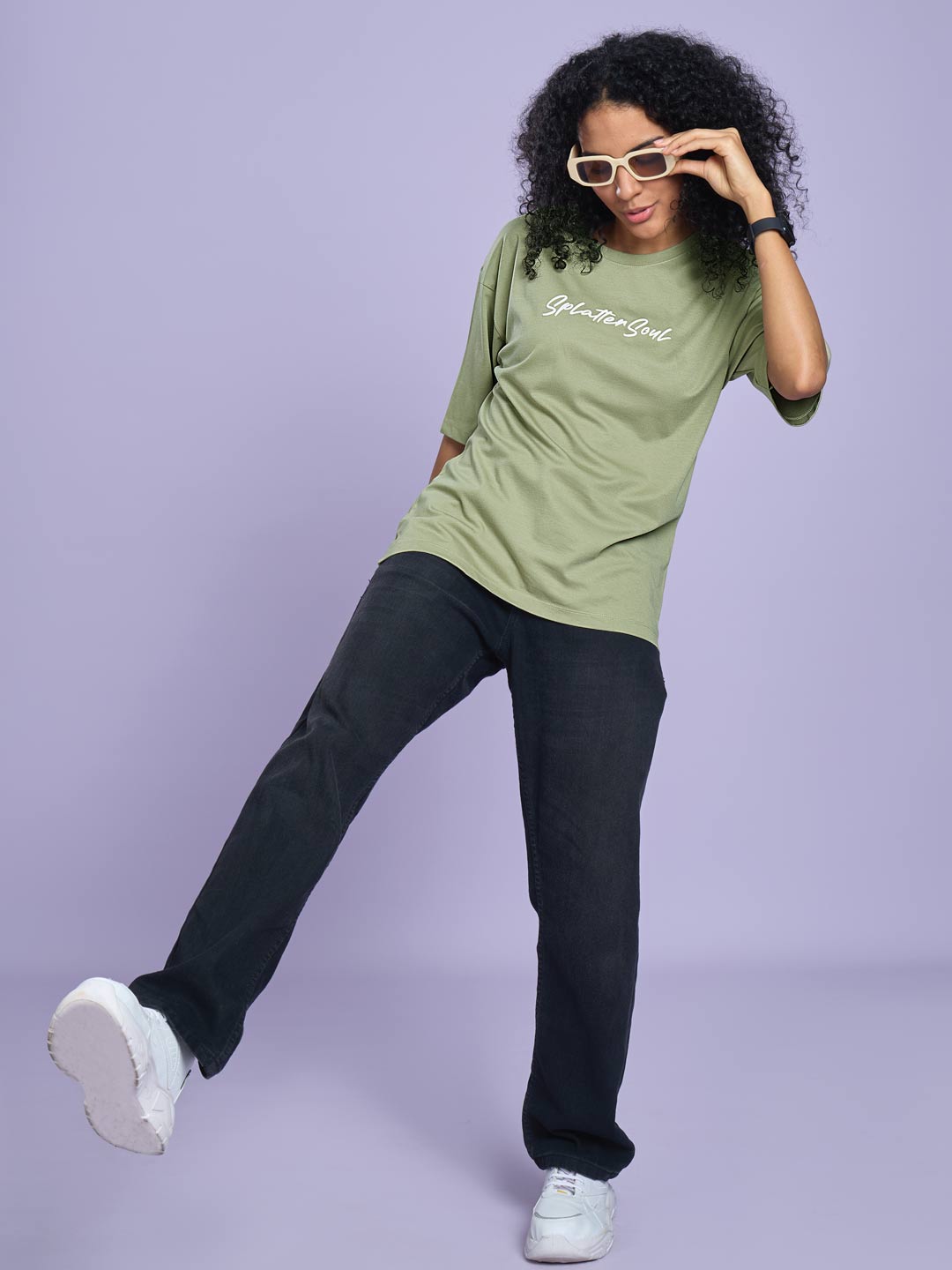 Woman wearing a green t-shirt and black pants against a purple background