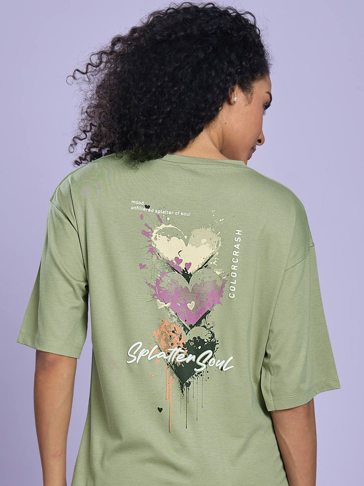 Person wearing a green t-shirt with a colorful design on the back against a purple background