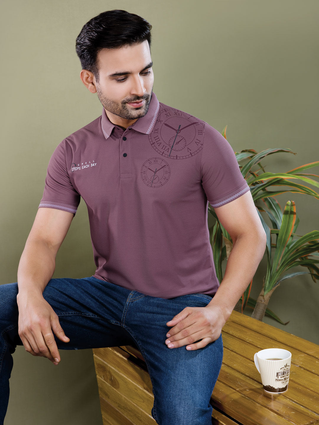 Man wearing a purple polo shirt sitting on a wooden bench with a plant in the background