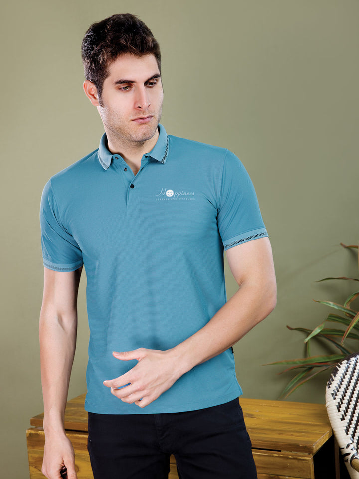 Man wearing a blue polo shirt with a logo against a green wall.