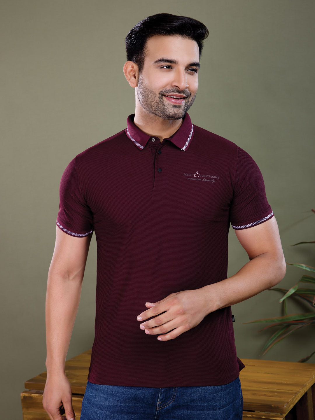 Man wearing a maroon polo shirt with a logo against a green background