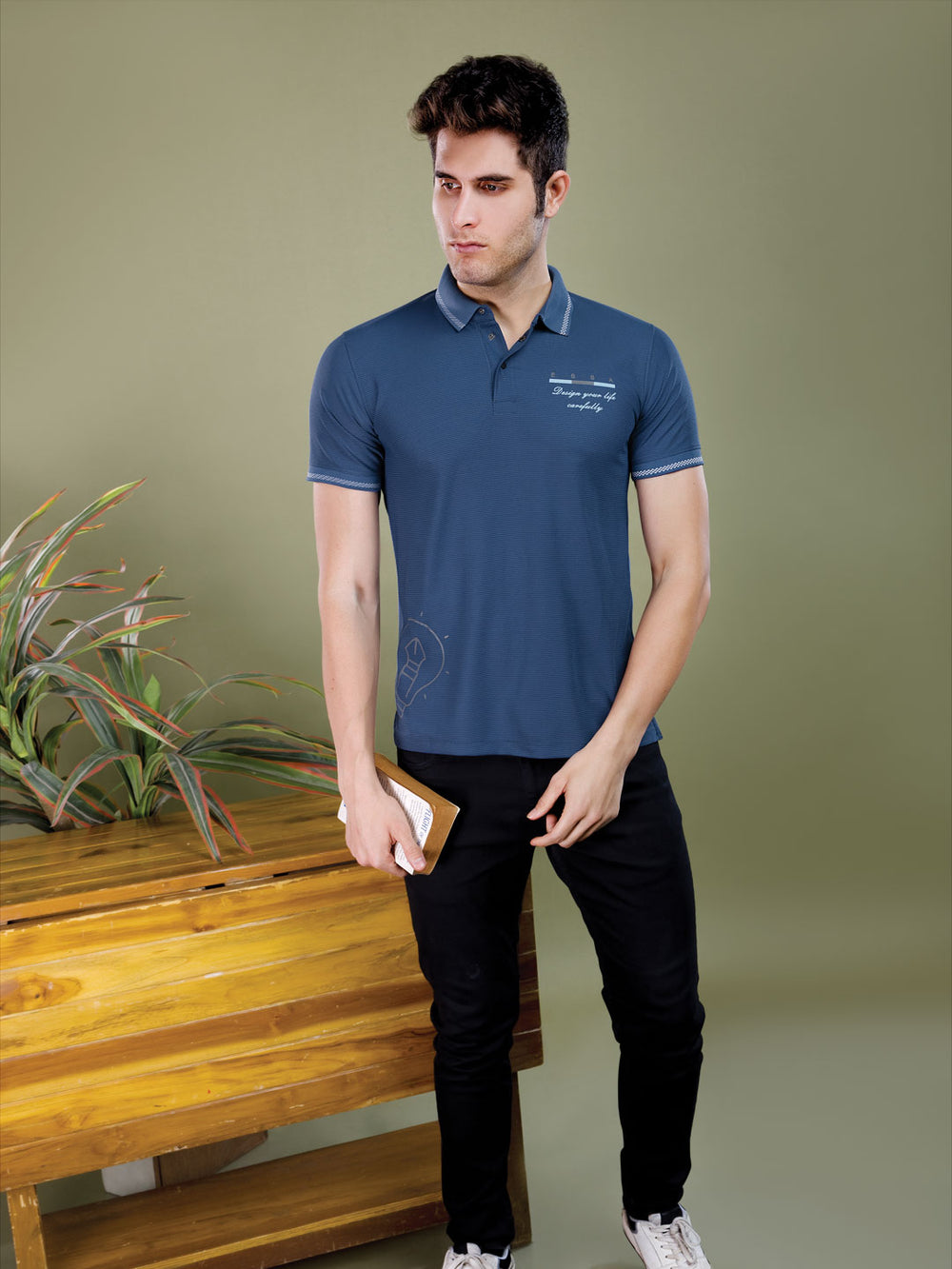 Man wearing a blue polo shirt with text, standing against a green wall.