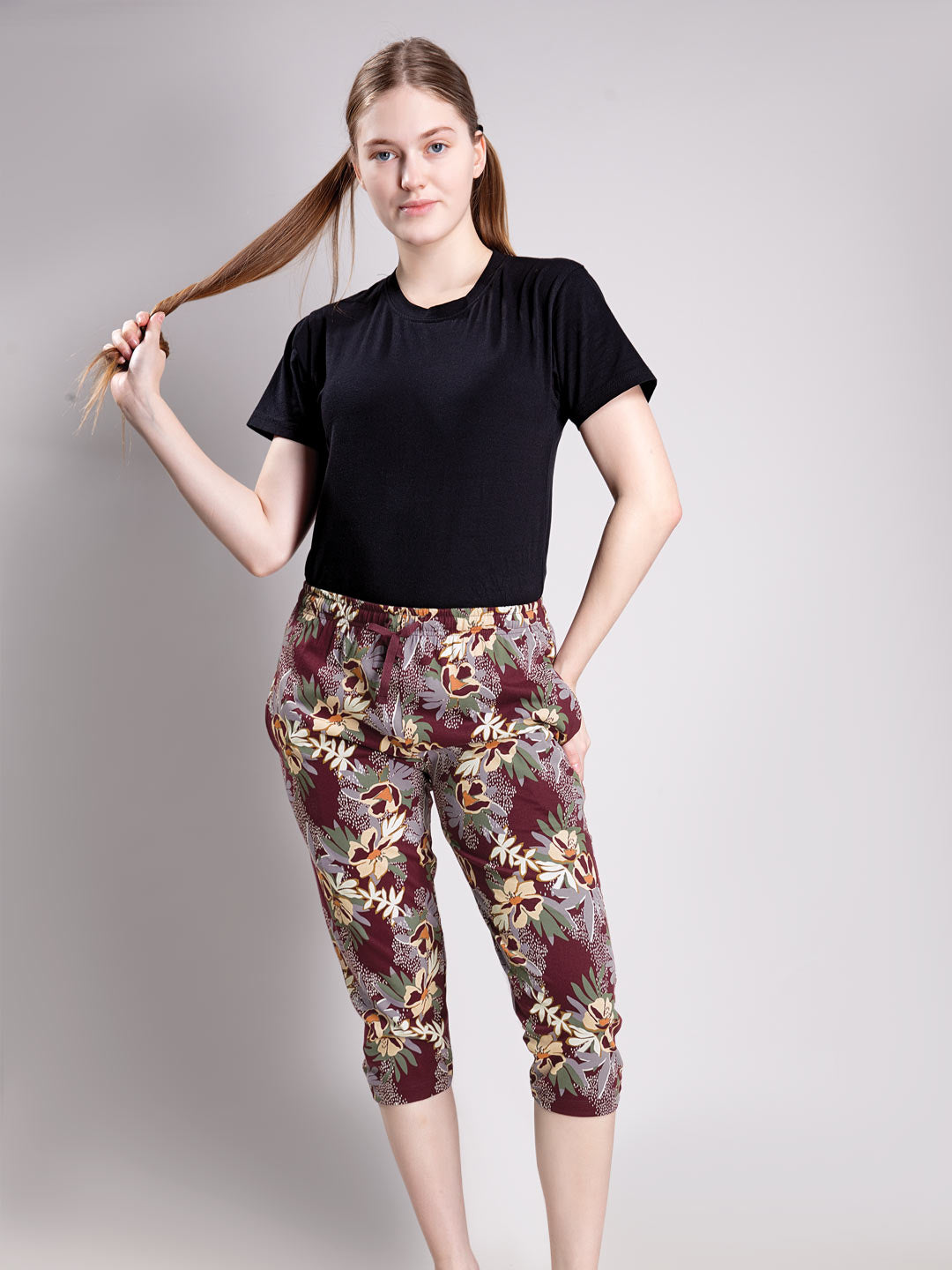 A woman modeling a black short-sleeve top and floral capri pants against a plain light gray studio background.