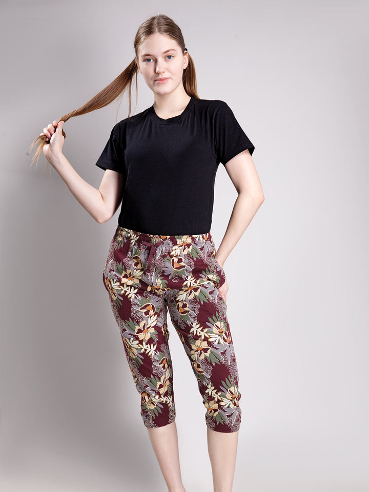 A woman modeling a black short-sleeve top and floral capri pants against a plain light gray studio background.