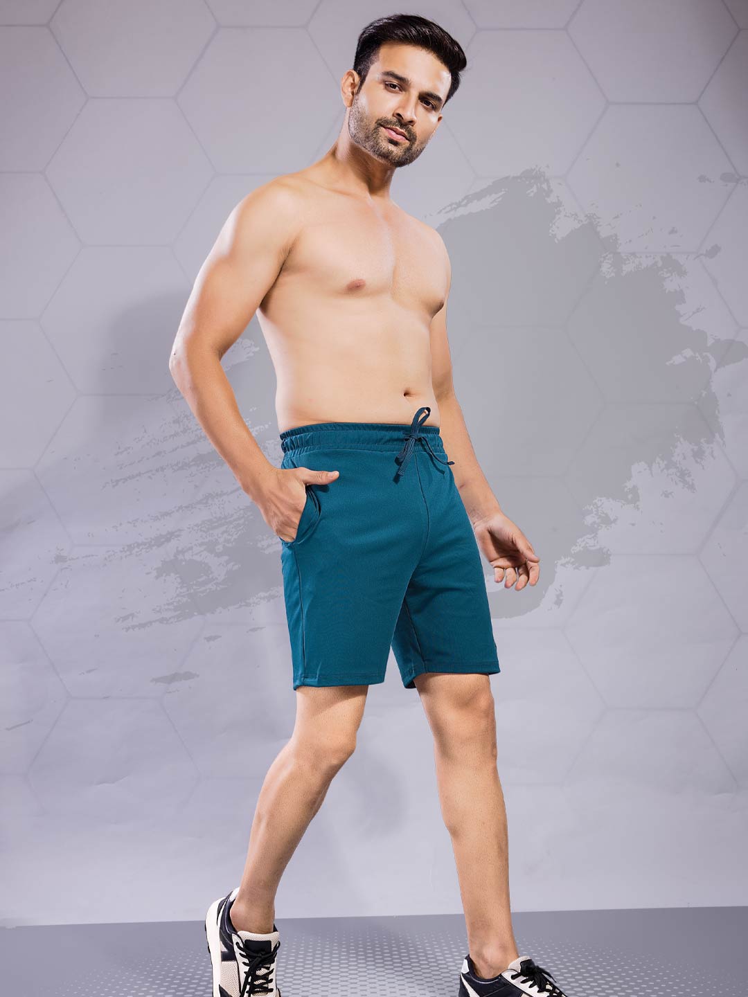 Man wearing teal shorts against a gray geometric background