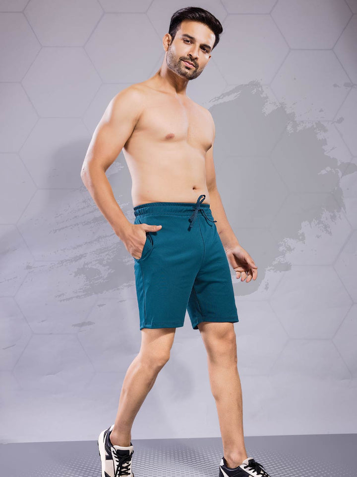 Man wearing teal shorts against a gray geometric background