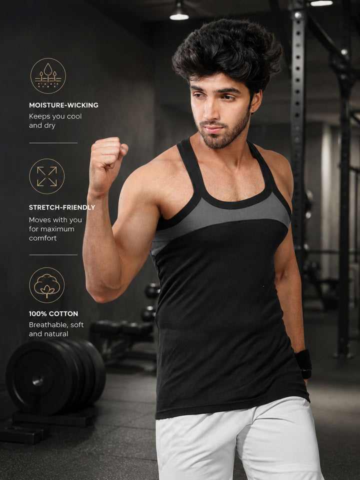 A man in a gym wearing a black and gray athletic tank top, with text overlays on the left highlighting its moisture-wicking, stretch-friendly, and 100% cotton qualities.#color_black