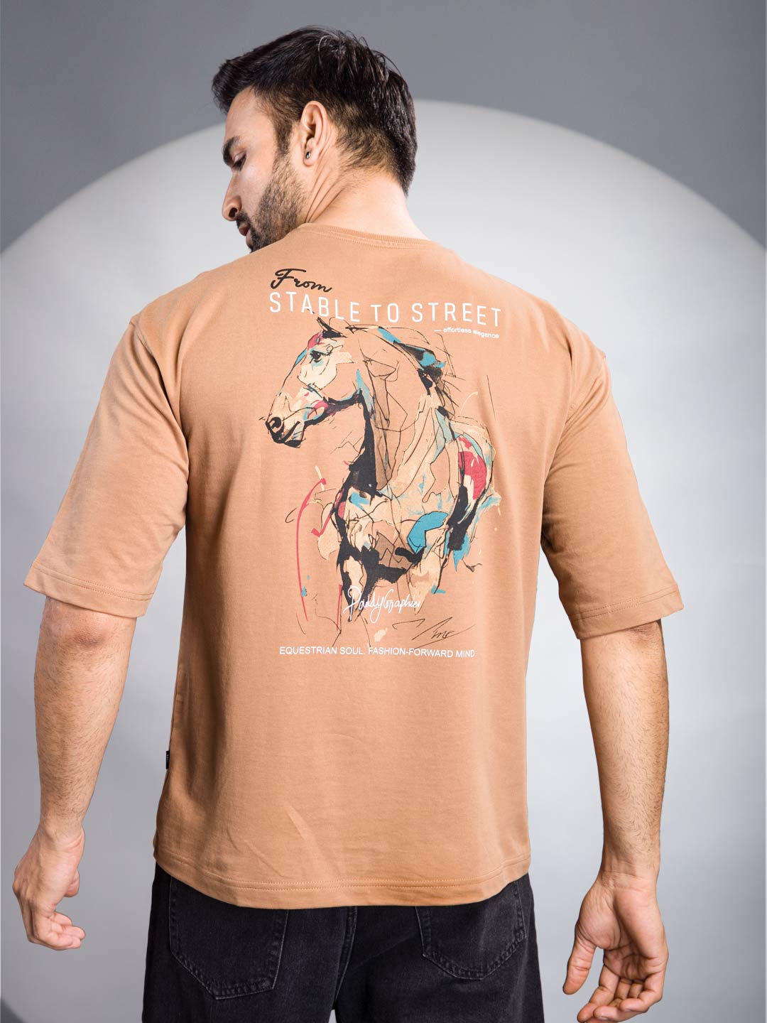 Man wearing a tan t-shirt with a horse graphic and text on the back against a gray background