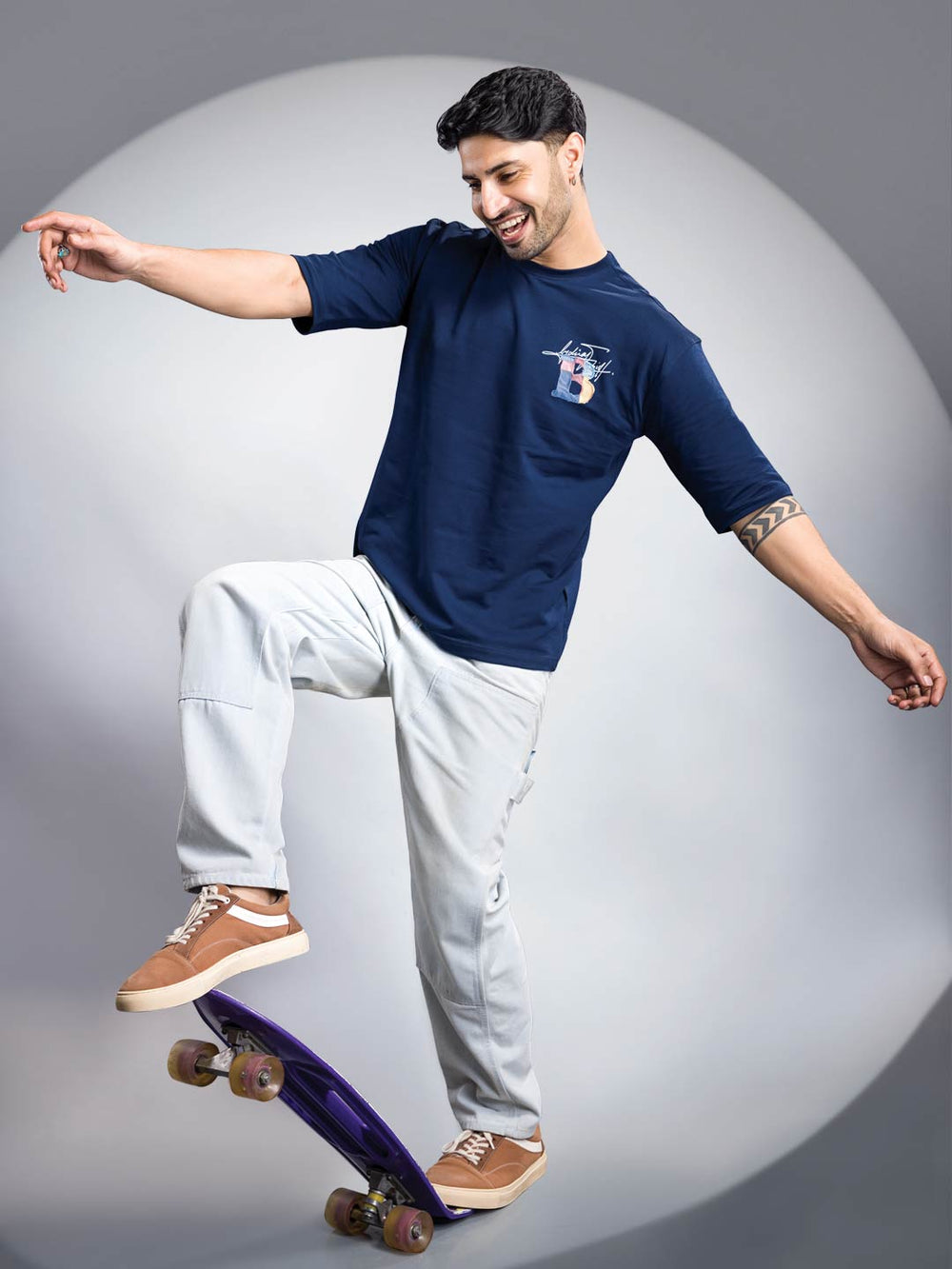 Man in navy blue t-shirt and light pants skateboarding on a gray background