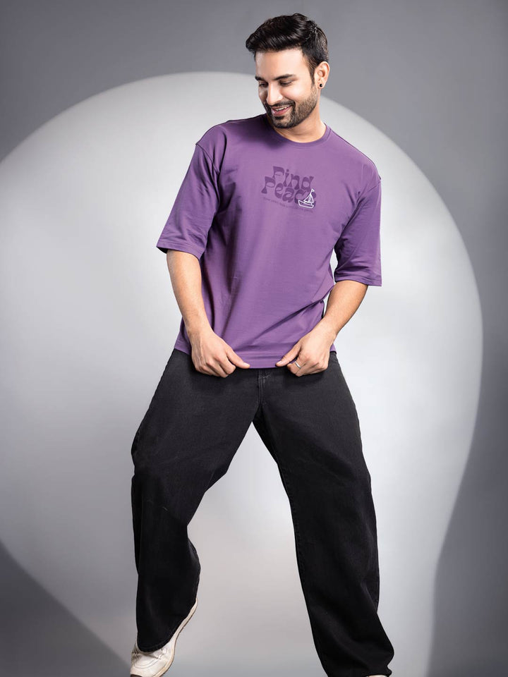 Man wearing a purple t-shirt with text and black pants on a gray background