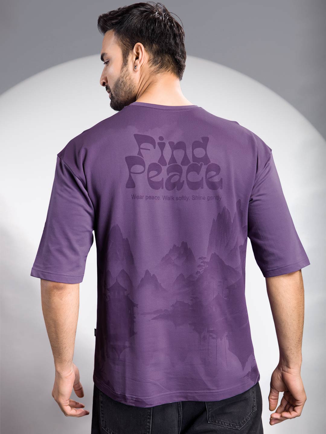 Man wearing a purple t-shirt with 'Find Peace' text on the back against a gray background