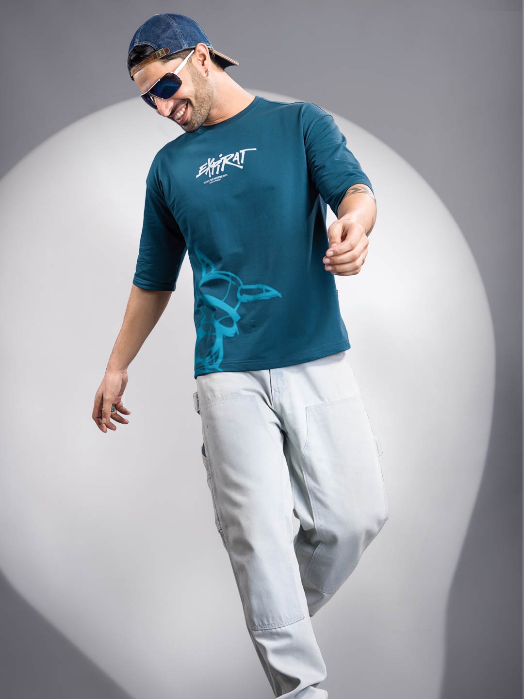 Man wearing a blue t-shirt with a logo and light gray pants on a gray background