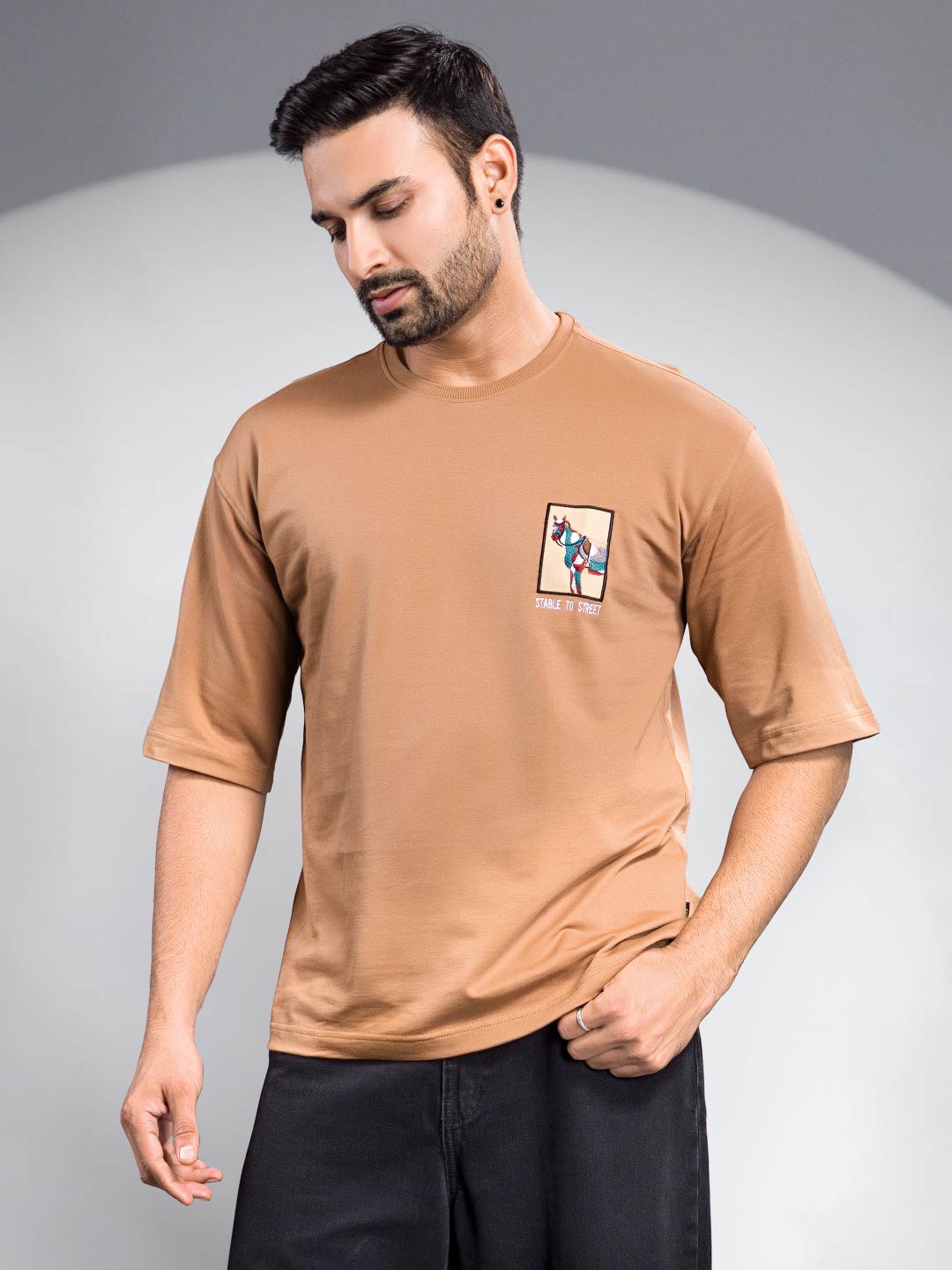 Man wearing a brown t-shirt with a small graphic on a gray background
