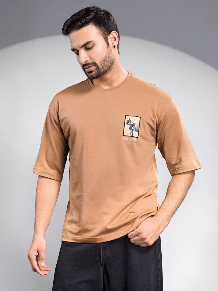 Man wearing a brown t-shirt with a small graphic on a gray background