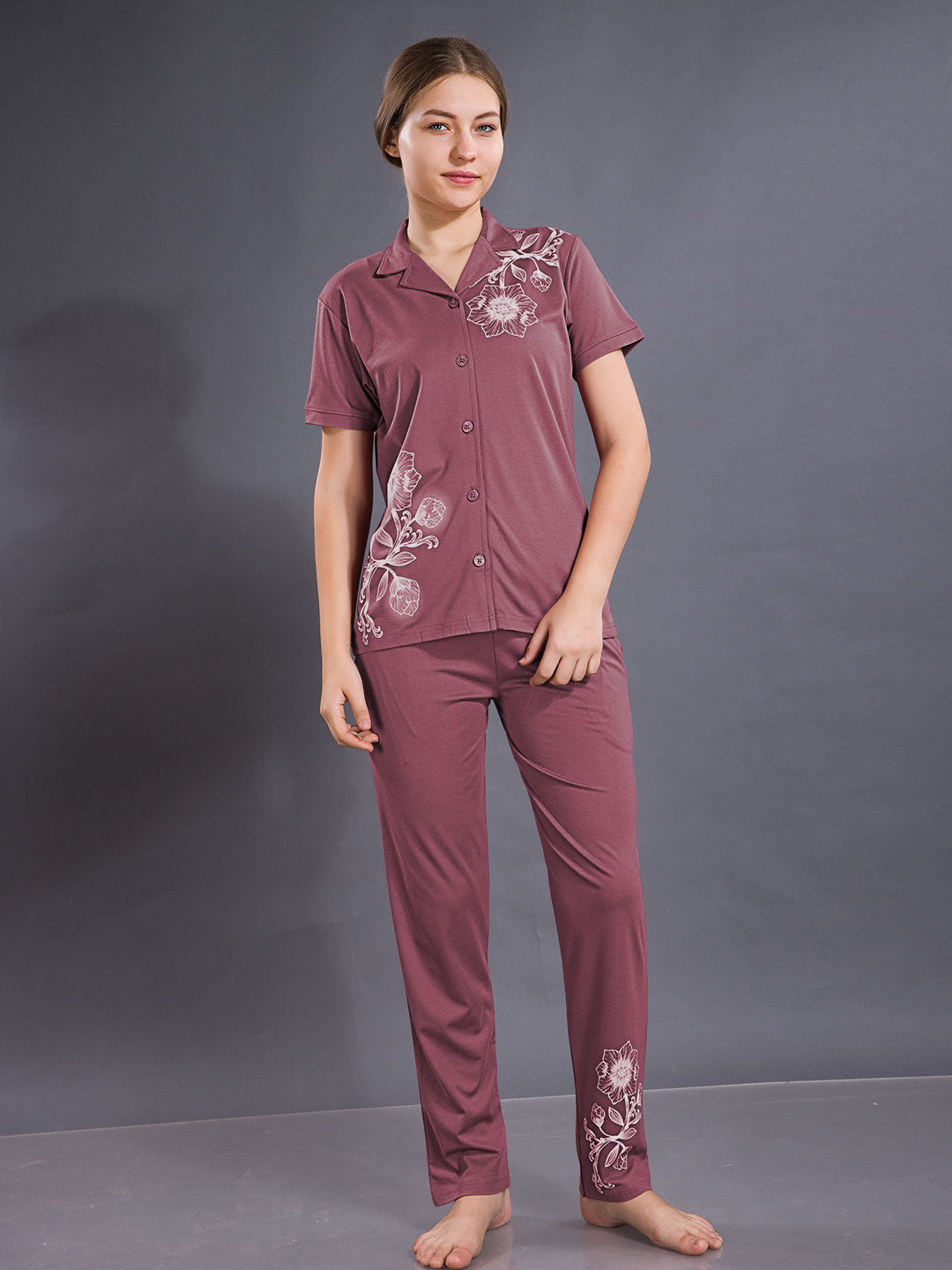 Woman wearing a maroon pajama set with floral embroidery against a gray background