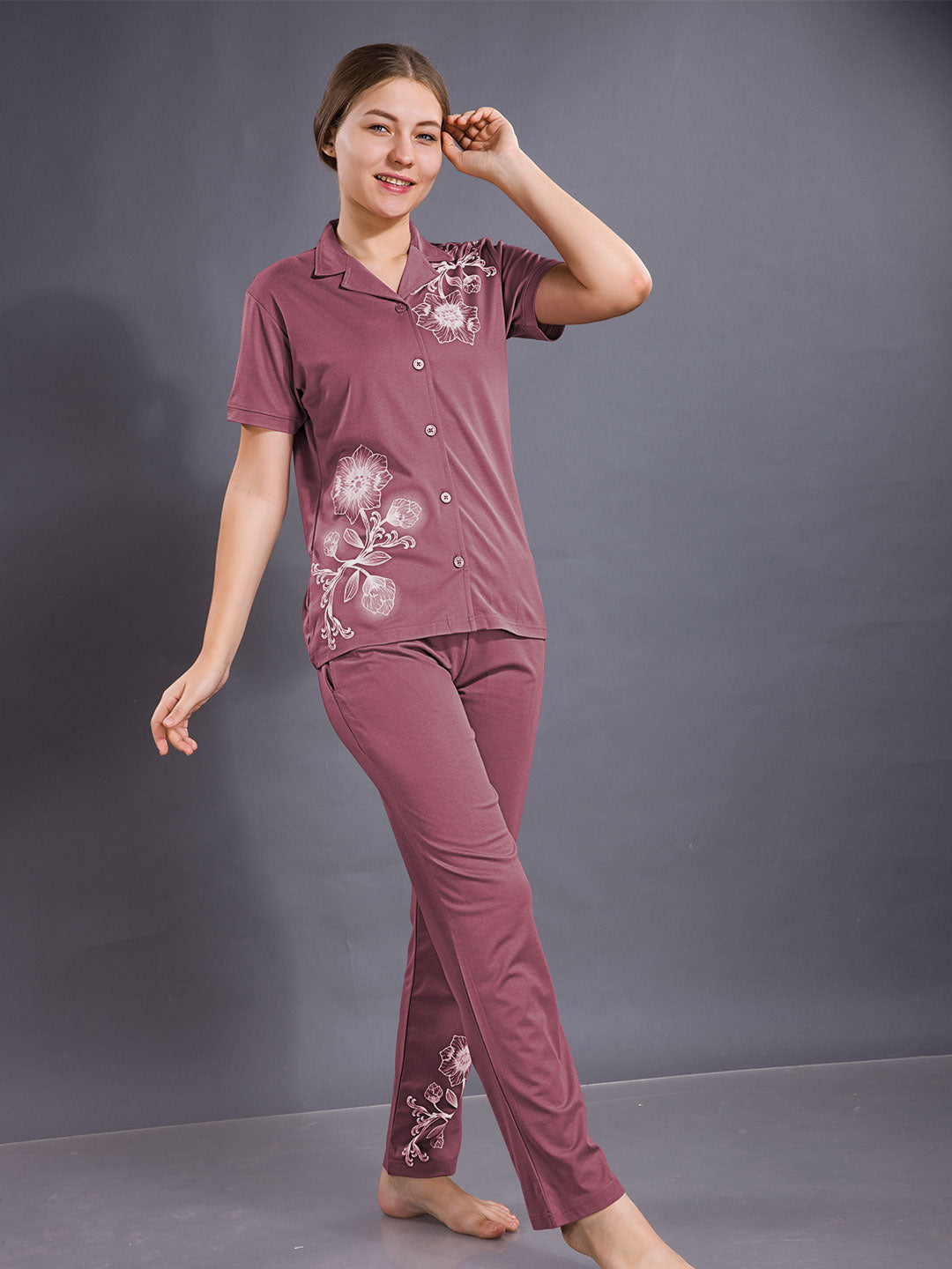 Woman wearing a maroon pajama set with floral patterns against a gray background