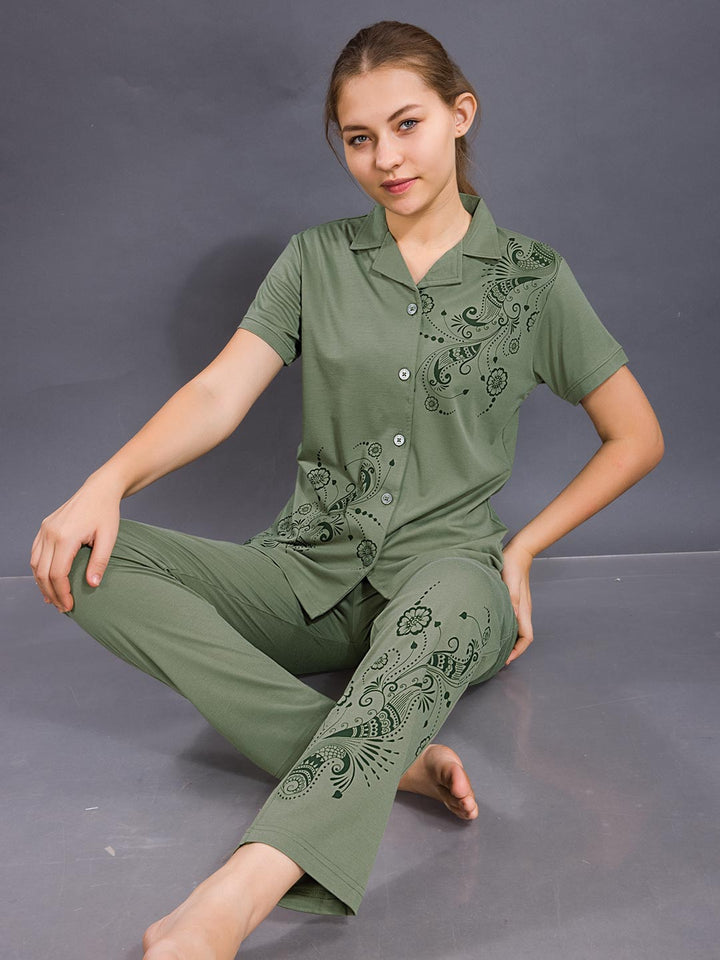 Woman wearing a green pajama set with intricate patterns on a gray background