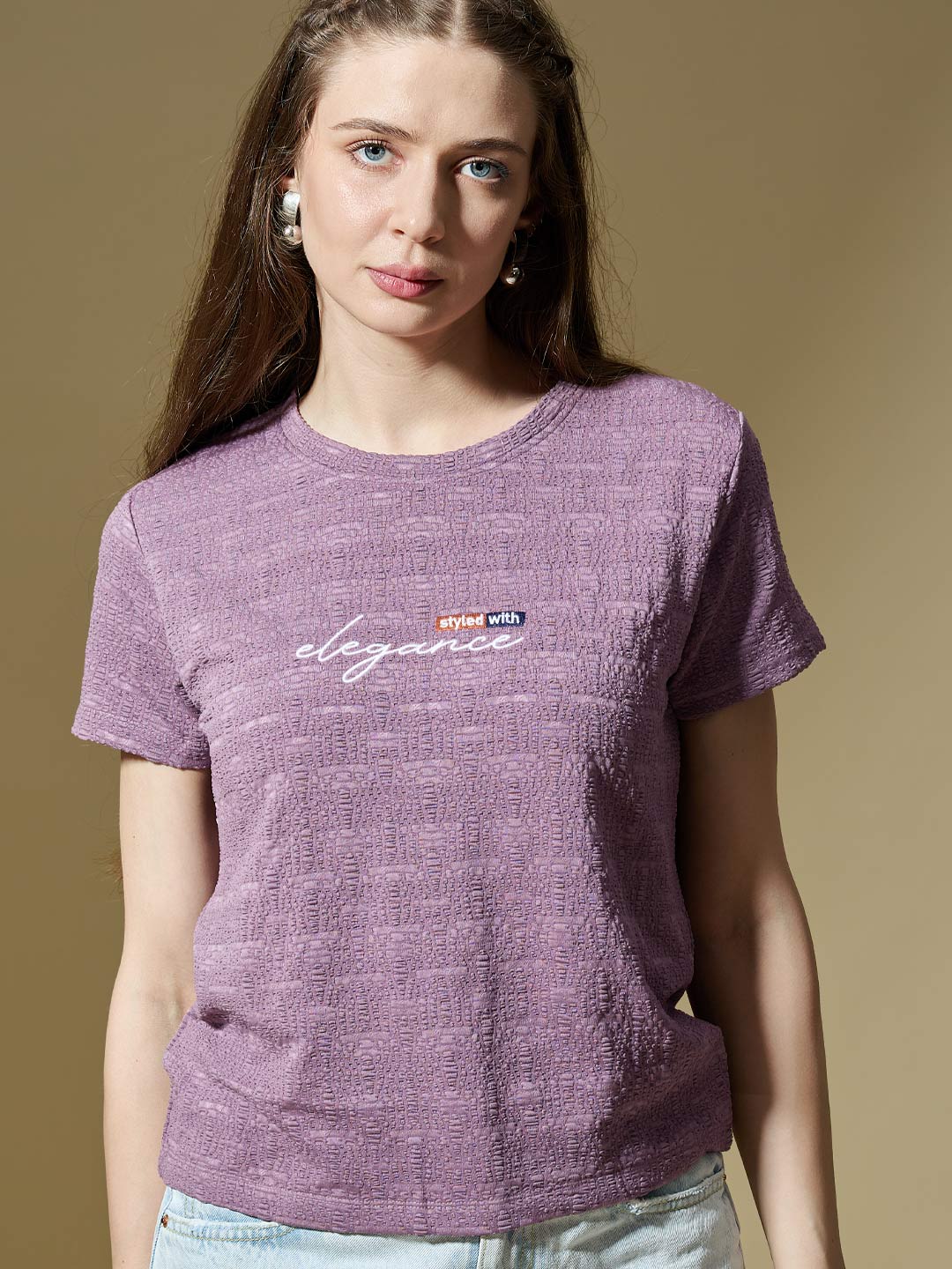 Woman wearing a purple t-shirt with a logo and text on a beige background