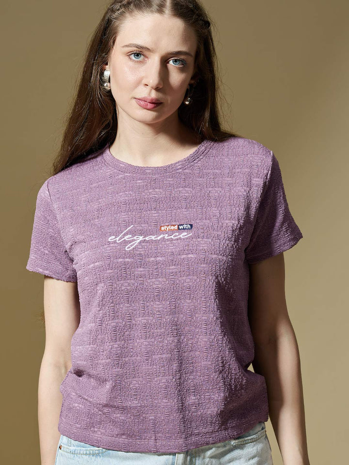 Woman wearing a purple t-shirt with a logo and text on a beige background
