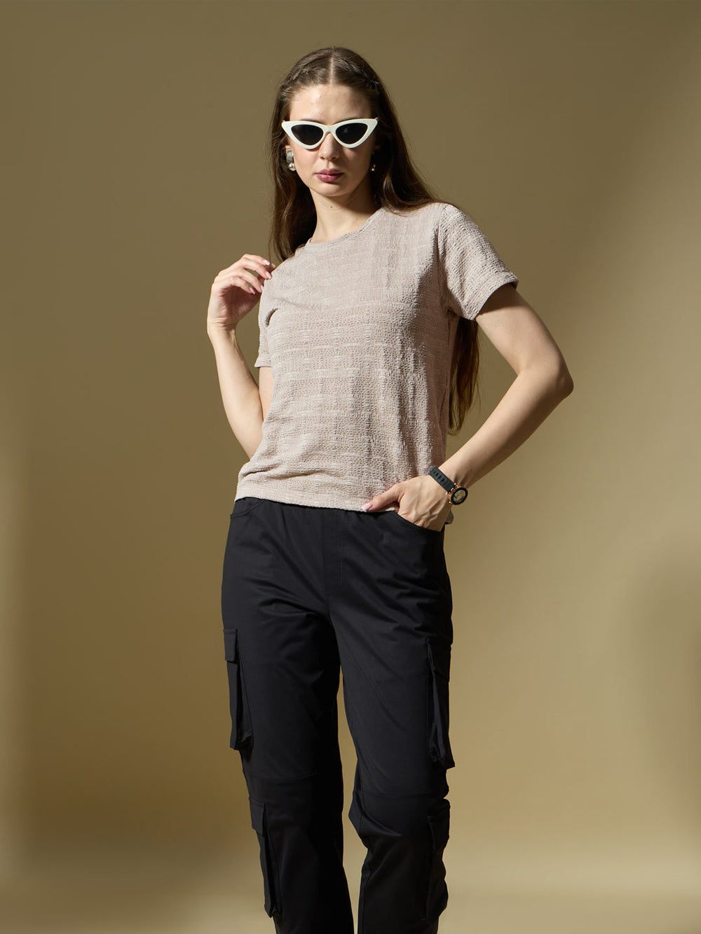 Woman wearing a beige textured shirt and black pants against a brown background