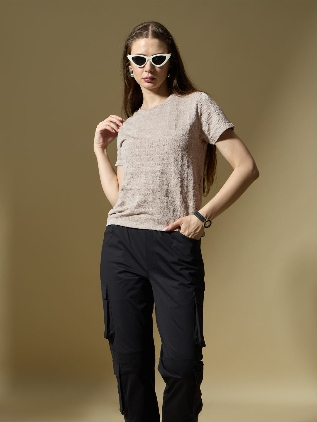 Woman wearing a beige textured shirt and black pants against a brown background