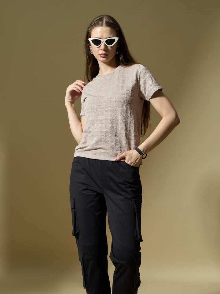 Woman wearing a beige textured shirt and black pants against a brown background