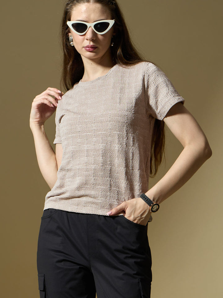 Woman wearing a beige textured top and black pants against a brown background