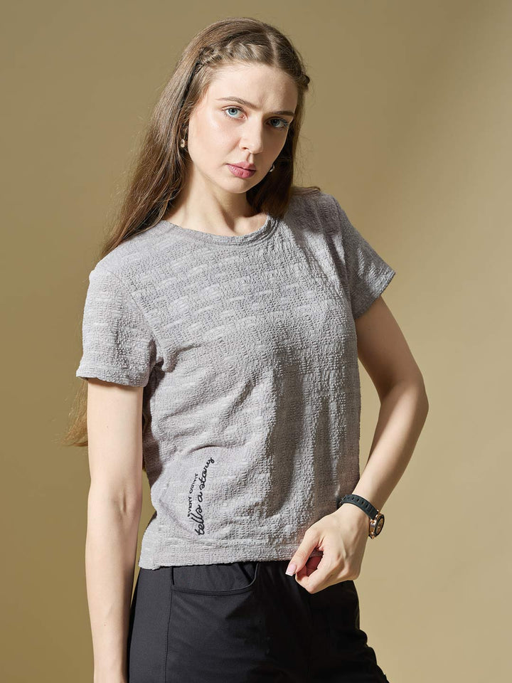 Woman wearing a textured gray t-shirt against a beige background