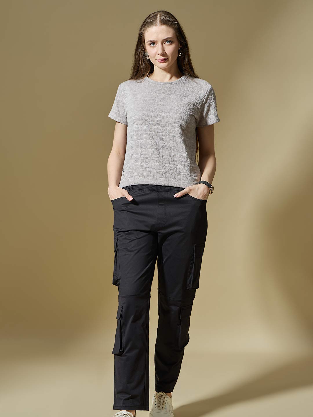 Woman wearing a gray t-shirt and black cargo pants against a beige background