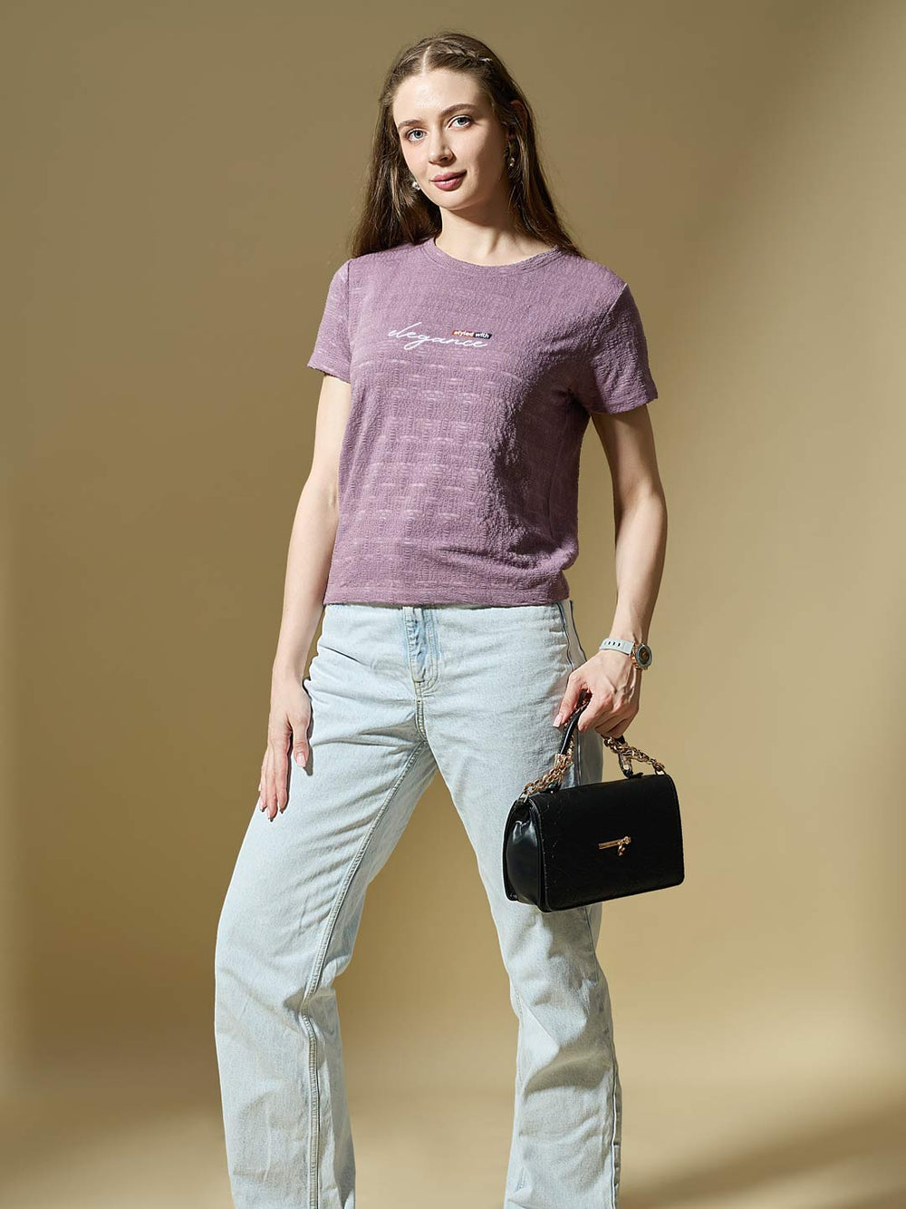 Woman wearing a purple t-shirt and light blue jeans, holding a black handbag on a beige background