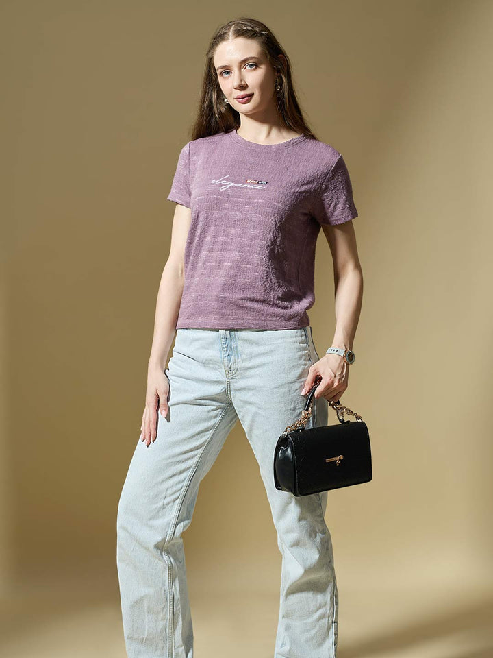 Woman wearing a purple t-shirt and light blue jeans, holding a black handbag on a beige background