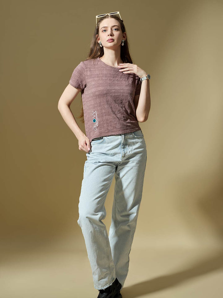 Woman wearing a brown t-shirt and light blue jeans against a beige background