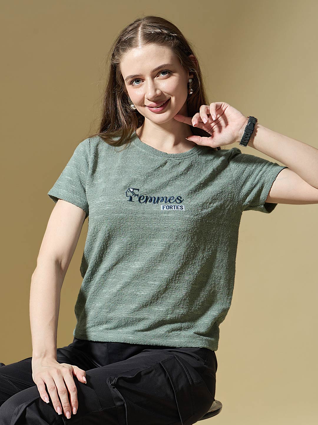 Woman wearing a green t-shirt with 'Femmes Fortes' logo on a beige background