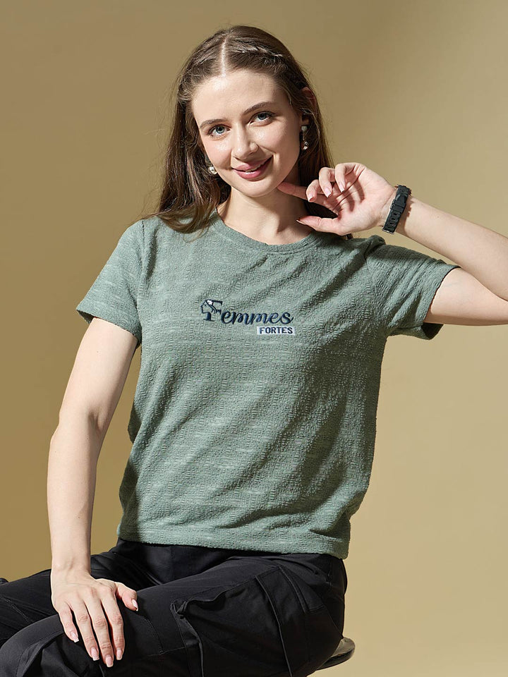 Woman wearing a green t-shirt with 'Femmes Fortes' logo on a beige background