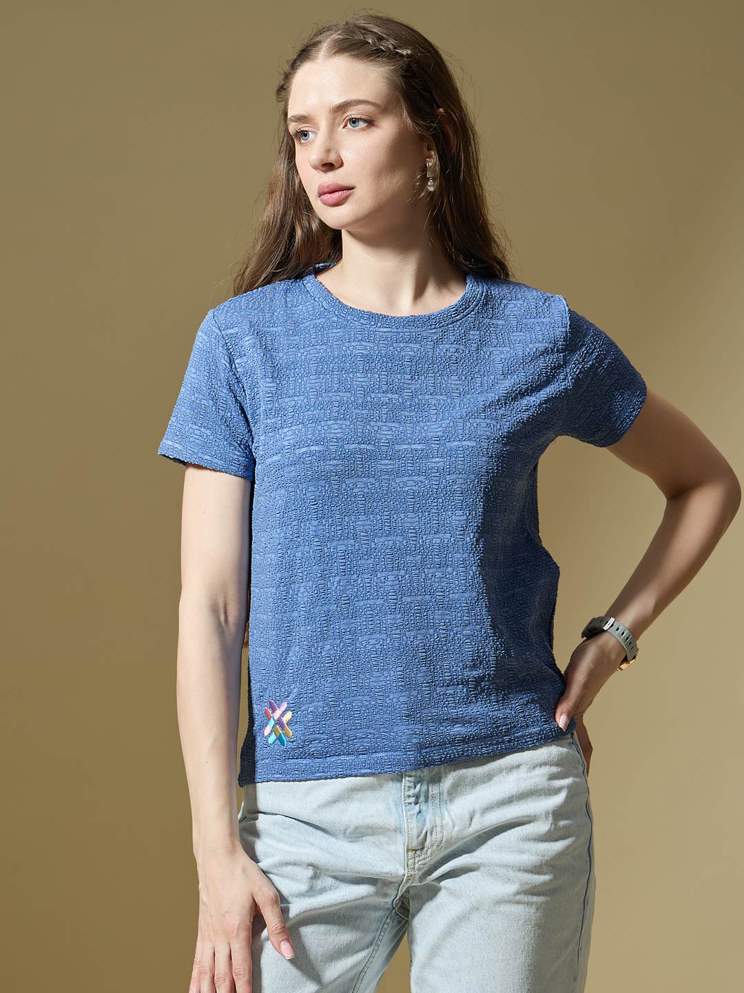 Woman wearing a blue textured t-shirt with a logo on a beige background