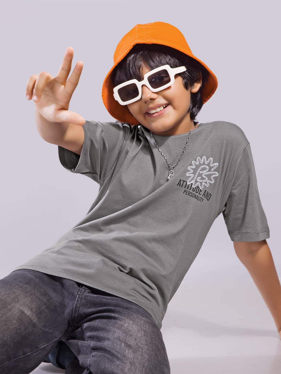 Child wearing a gray t-shirt with a logo, orange bucket hat, and white sunglasses on a light gray background boys printed down shoulder t-shirt #color_dove-grey
