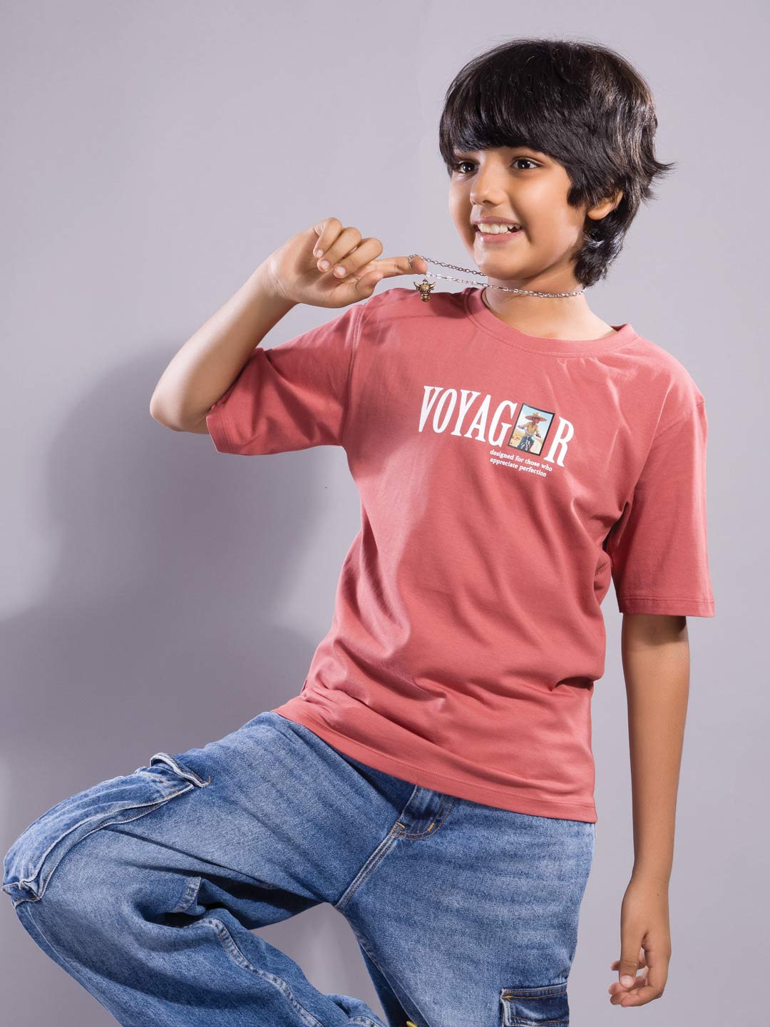 Child wearing a light red 'Voyager' t-shirt and blue jeans on a gray background