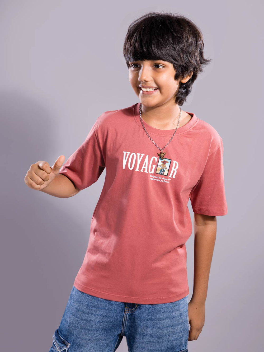 Child wearing a light red 'Voyager' t-shirt on a gray background