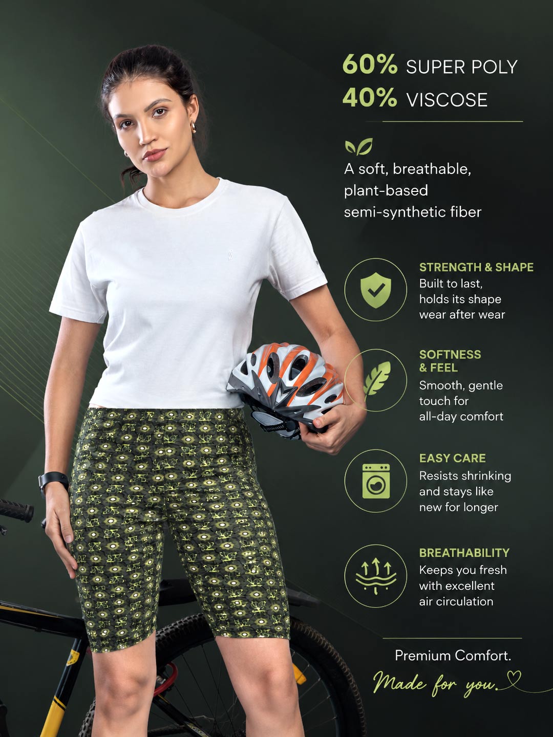 A woman modeling patterned green and black bike shorts with a white t-shirt, holding a bicycle helmet against a dark green background with product feature callouts.