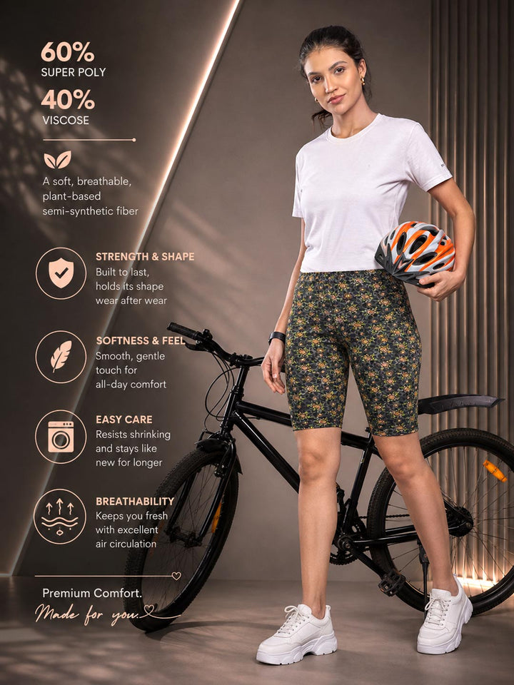 A woman stands beside a bicycle wearing patterned green bike shorts, a white T-shirt, and white sneakers, holding an orange and black bicycle helmet. Text on the left describes the shorts' material and benefits.