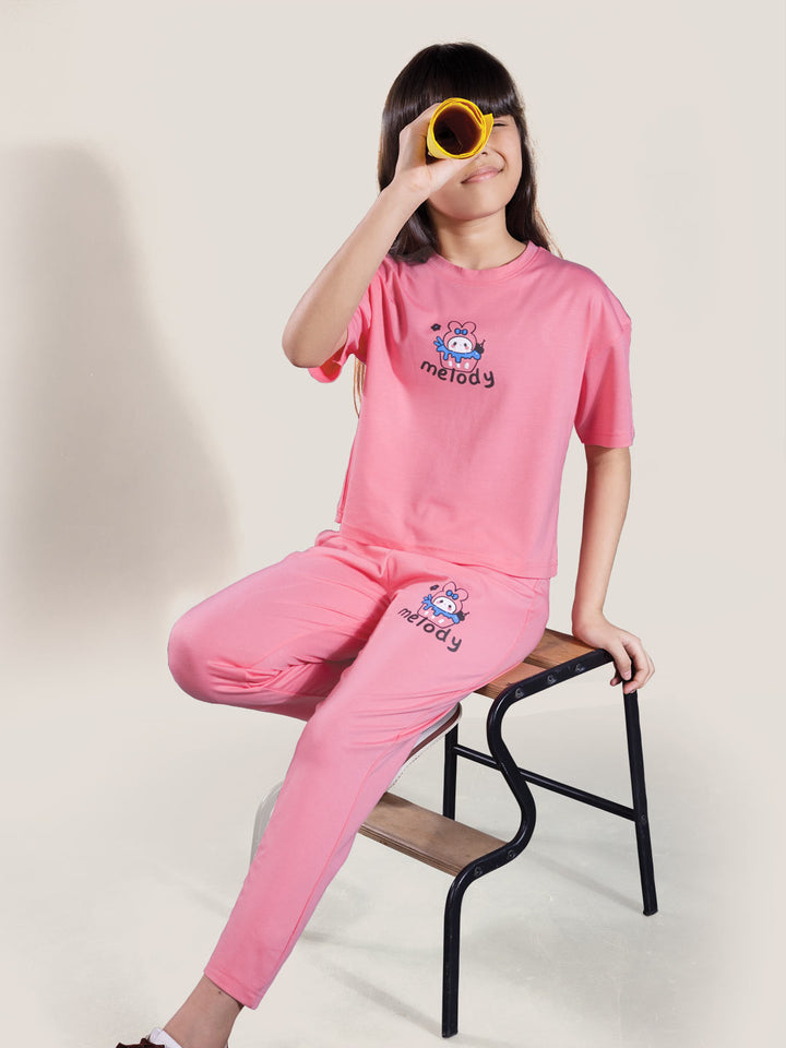 Person wearing a pink outfit with a brand logo, sitting on a chair against a plain background