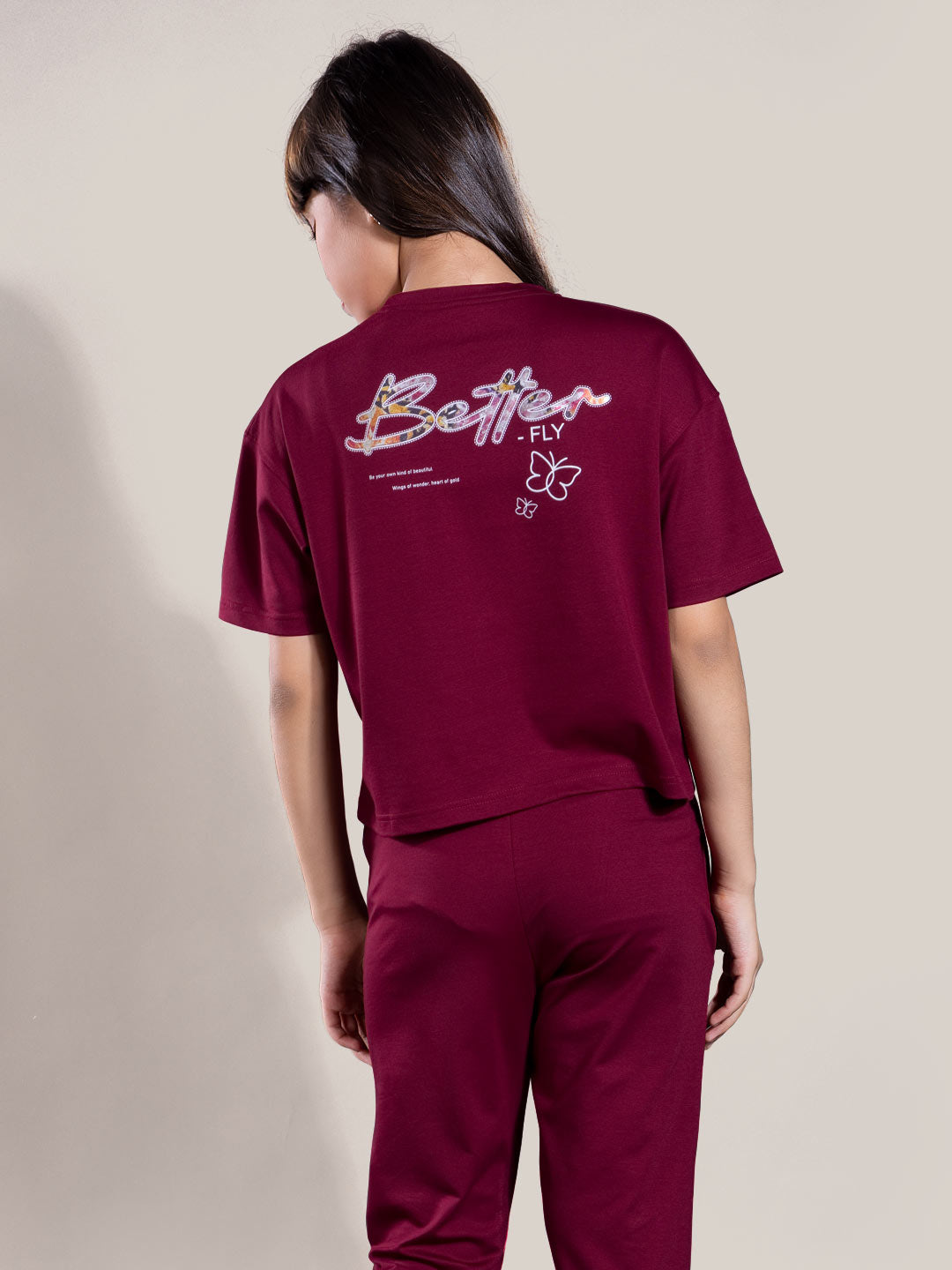 Person wearing a maroon outfit with 'Better Fly' text on the back against a beige background