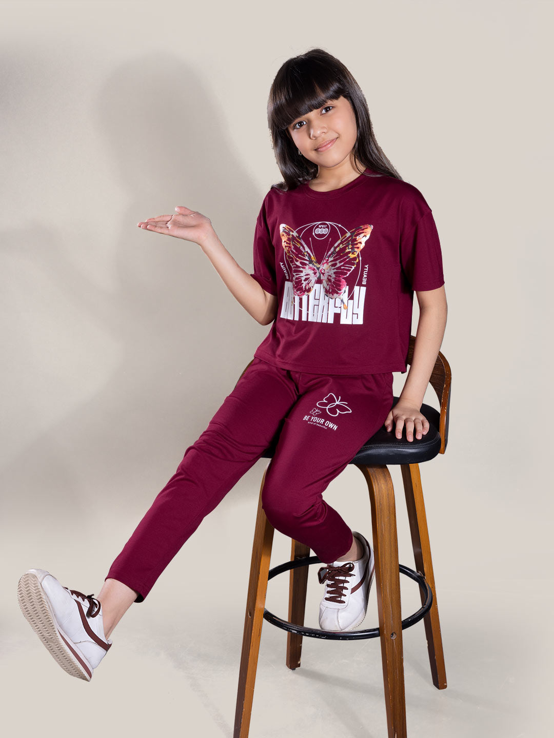 Child wearing a maroon outfit with a graphic design on a stool against a plain background