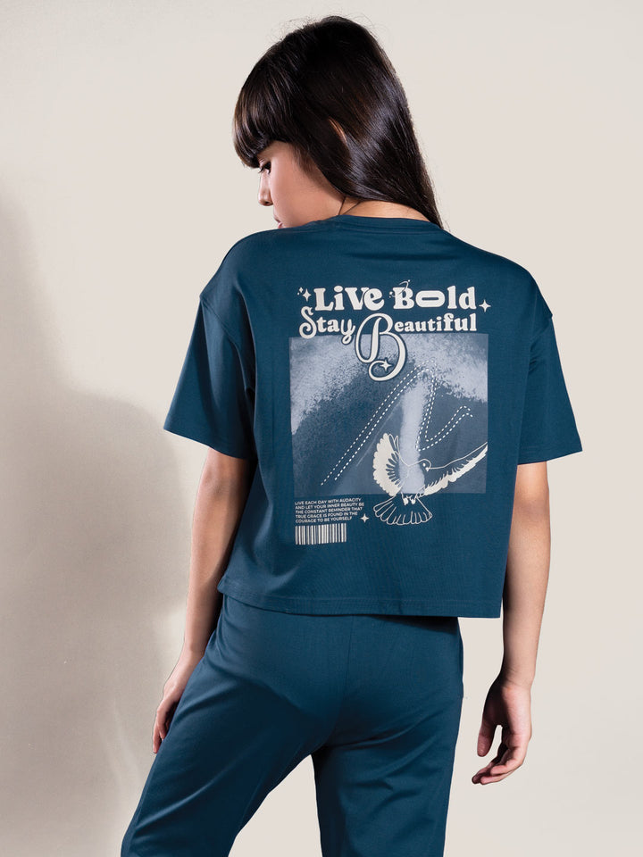 Person wearing a teal t-shirt with 'Live Bold Stay Beautiful' text on the back.