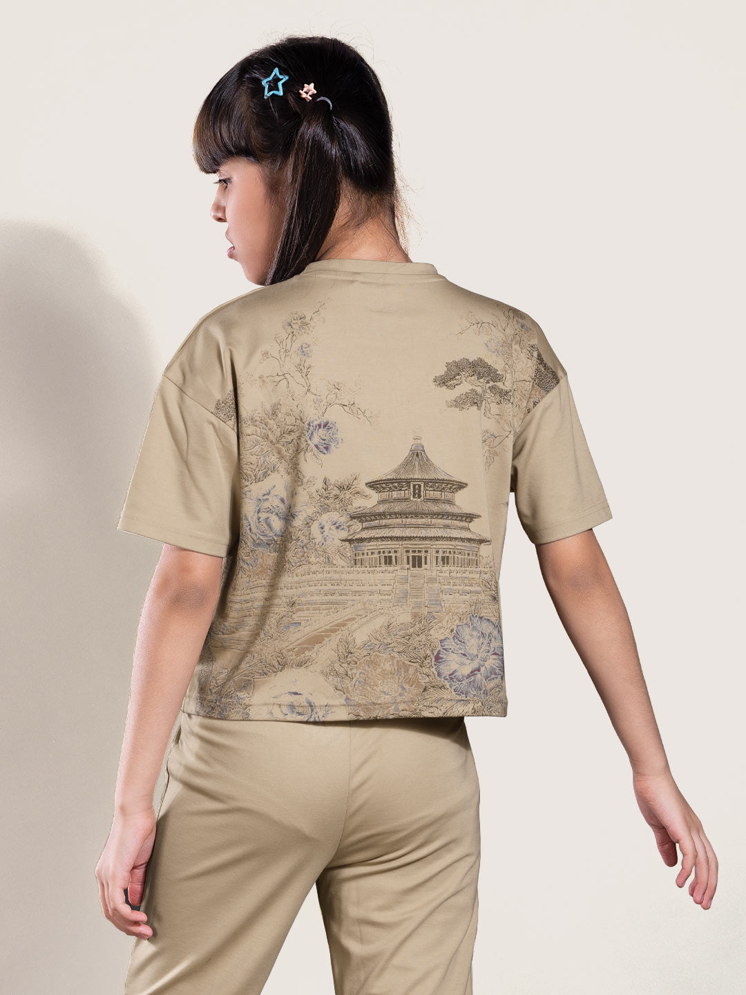 Person wearing a beige outfit with a traditional design on the back against a plain background