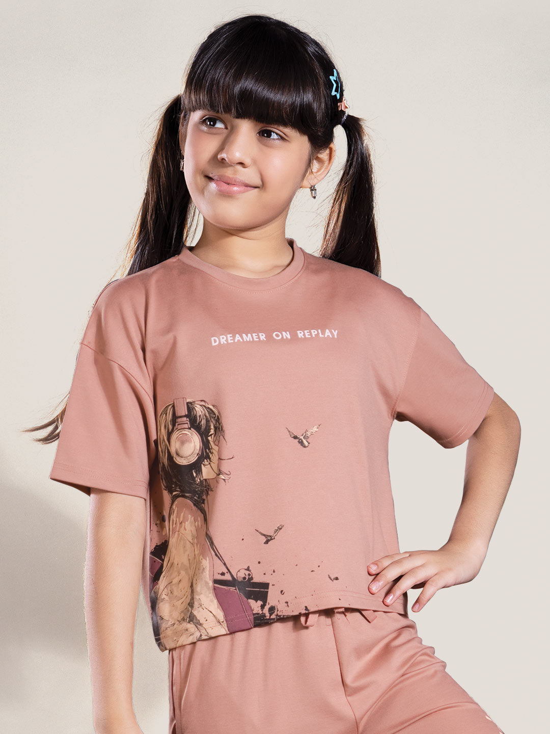 Young girl wearing a pink t-shirt with graphic design and text on a plain background