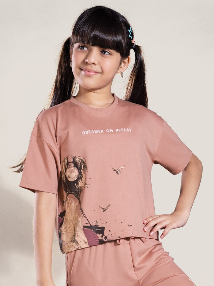 Young girl wearing a pink t-shirt with graphic design and text on a plain background