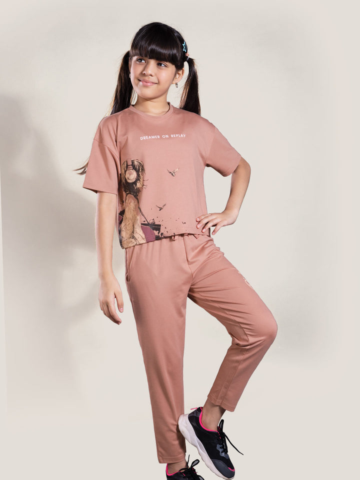 Young girl wearing a pink outfit with a graphic design on a plain background