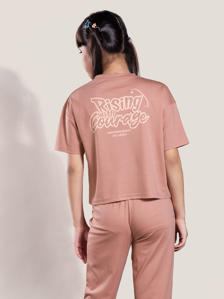 Person wearing a pink outfit with 'Rising with Courage' text on a plain background